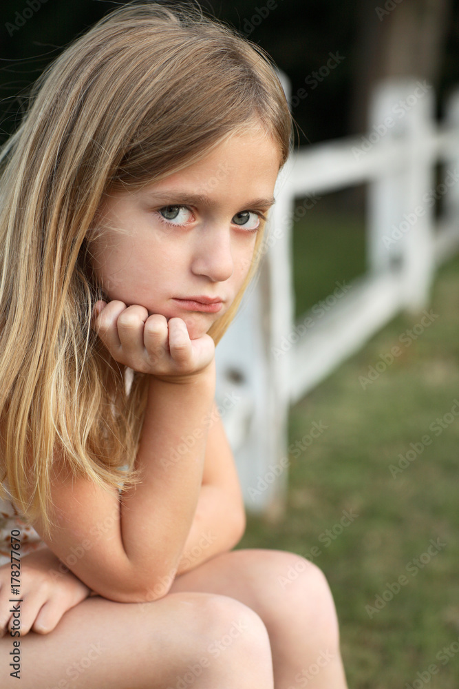 Young girl with long hair sitting outdoors with serious expression Young girl with long hair sitting outdoors with serious expression