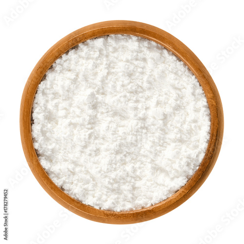 Powdered sugar in wooden bowl. Unsifted finely ground white refined sugar. Also called confectioners or icing sugar and icing cake. Isolated macro food photo close up from above on white background.