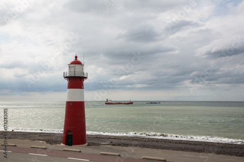 red and white historical lighthouse, atmospheric sky, ship in background