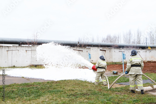 Firefighters extinguish the fire with a chemical foam coming from the fire engine through a hose