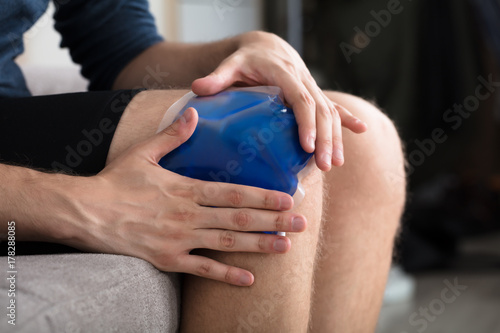 Person Sitting And Applying Ice Gel Pack On Knee photo
