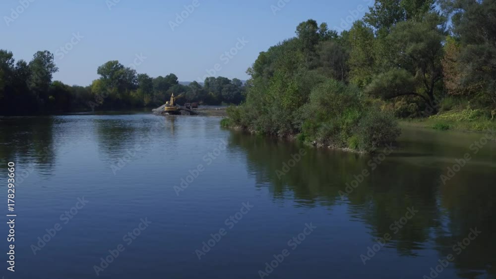 Aerial view of river flow with forest riverbank during two yellow dredges shoveling sand, excavator loading tipper truck, backhoe scooping and pouring gravel on sandbank, sunny day, blue sky Aerial view of river flow with forest riverbank during two yellow dredges shoveling sand, excavator loading tipper truck, backhoe scooping and pouring gravel on sandbank, sunny day, blue sky