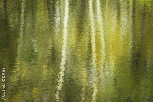 Autumn reflections create colorful abstract patterns on the surface of a small woodland pond on a warm October day.