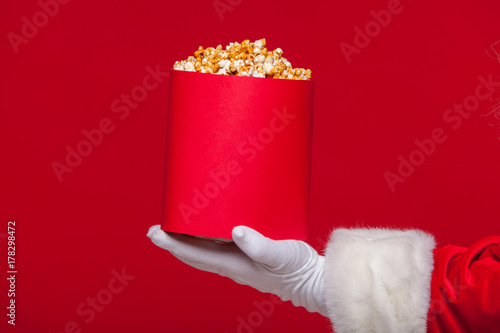 Christmas. Photo of Santa Claus gloved hand With a red bucket with popcorn, on a red background
