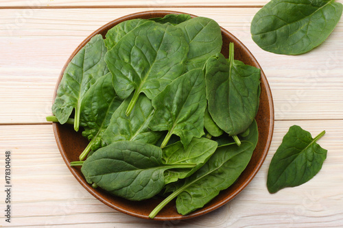 spinach leaves in bowl on white wooden table top view