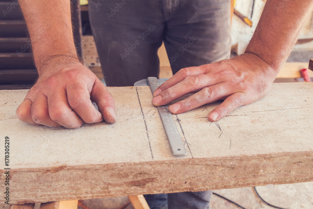 Carpenter usign ruler on raw plank in garage. Carpenter usign ruler on raw plank in garage.