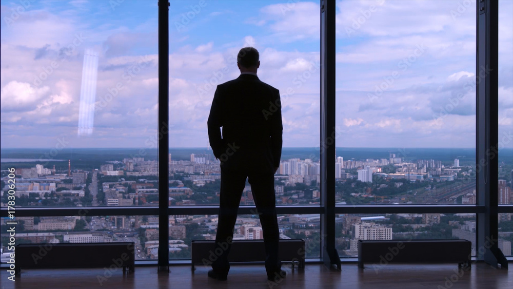 Fototapeta premium Businessman standing near the window and looking into it. Man stands near the stained glass