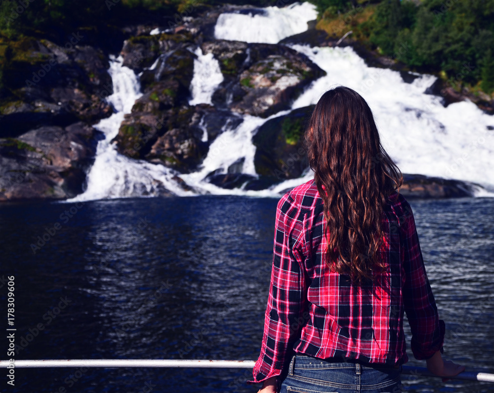 Young woman with long hair and red shirt looking at Hellesyltfossen, a waterfall in Hellesylt, Norway