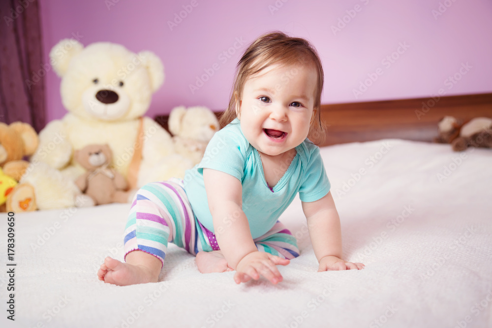 Cute smiling little baby girl sitting on the bed with soft toys. Seven month old infant child on white soft blanket Cute smiling little baby girl sitting on the bed with soft toys. Seven month old infant child on white soft blanket