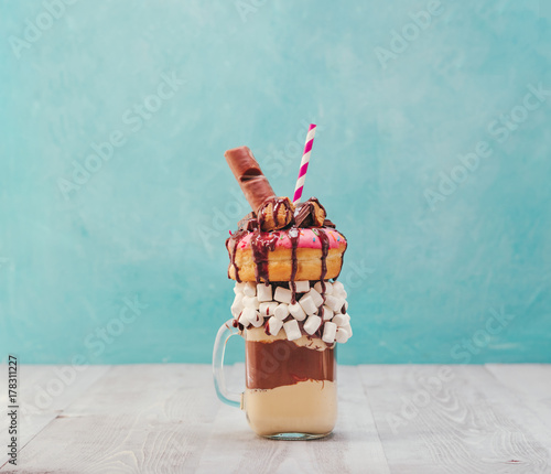 Photo Chocolate and donuts extreme milkshake with marshmallow and other sweets in mason jar on gray wooden table and blue background