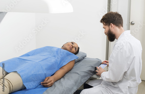 Woman Looking At Male Doctor Examining Her At Clinic