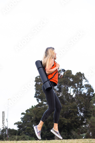 blonde woman at the park with yoga mat and bottle of water in black leggings