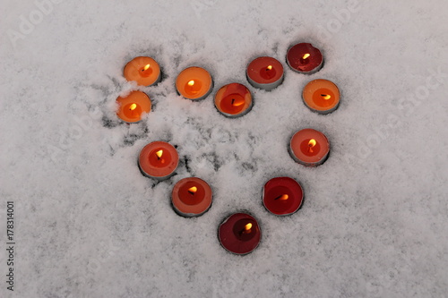 bright multicolored burning candles lined in the shape of a heart in the snow