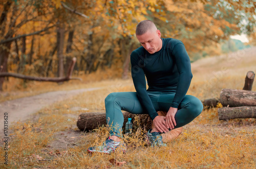  young athlete runner sits on a log holding an ankle with his hands after cramping