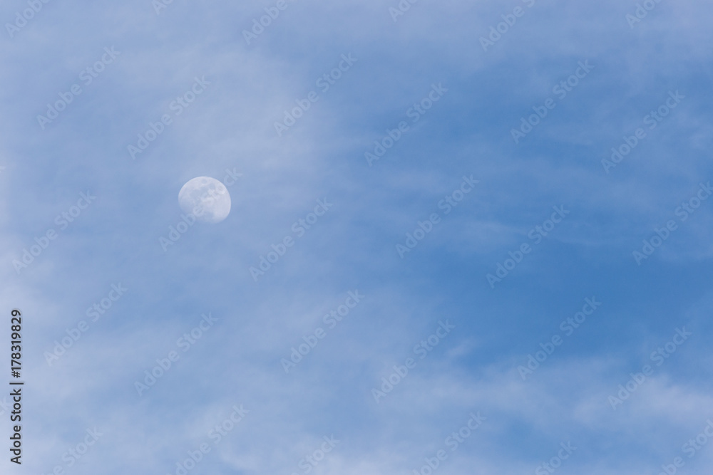 View of the moon through some clouds in the blue sky View of the moon through some clouds in the blue sky