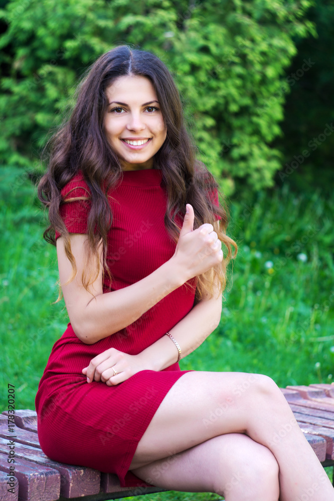 Beautiful girl sitting on a bench in a red dress and poses for the camera Beautiful girl sitting on a bench in a red dress and poses for the camera
