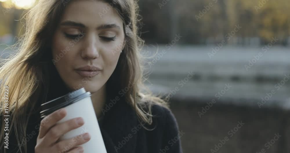 close-up portrait attractive young girl looks at the sunrise on the river and drinking coffee from a paper cup