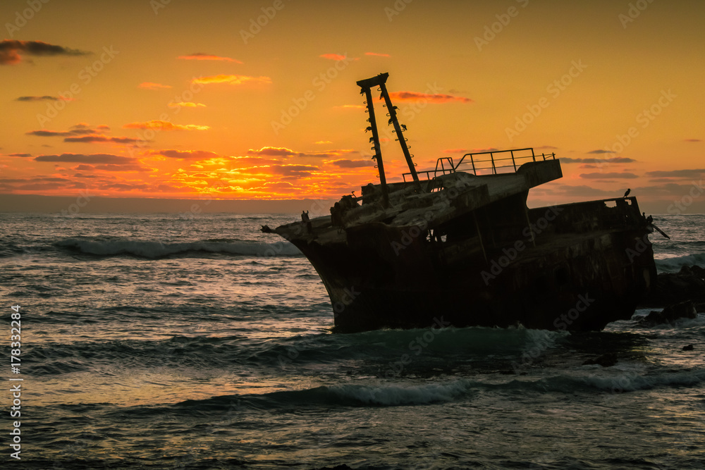 The wreck of a trawler lies on the rocks silhouetted against the golden light of sunset. Cape Agulhas, South Africa The wreck of a trawler lies on the rocks silhouetted against the golden light of sunset. Cape Agulhas, South Africa