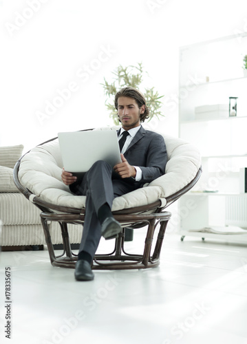 young businessman with laptop sitting in big comfortable armchair.