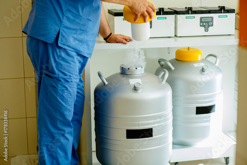 Closeup of male technician holding rack in nitrogen tank. Cryosample taken out of Liquid Nitrogen cryostorage in laboratory. photo