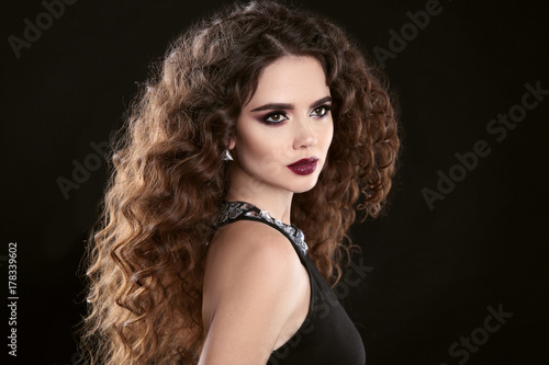 Hairstyle. Fashion brunette girl with Long curly hair  beauty makeup. Glamour portrait of beautiful woman with marsala matte lips isolated on black background.