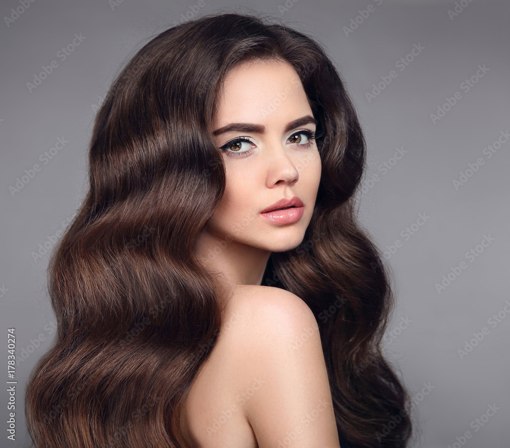 Naklejka premium Beauty hair. Brunette girl portrait with long shiny wavy hair. Beautiful model with healthy hairstyle and clean makeup isolated on studio dark background. Shampoo care product.