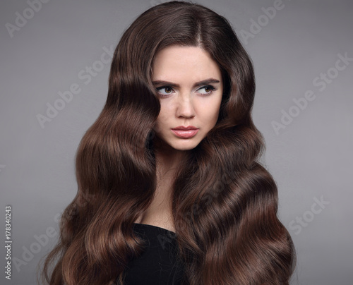 Beauty hair. Brunette girl portrait with long shiny wavy hair. Beautiful model with healthy hairstyle and clean makeup isolated on studio dark background. Shampoo care product.