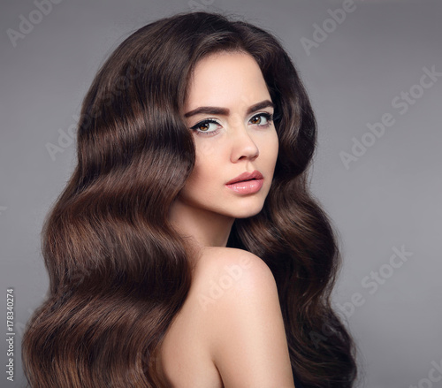 Beauty hair. Brunette girl portrait with long shiny wavy hair. Beautiful model with healthy hairstyle and clean makeup isolated on studio dark background. Shampoo care product.
