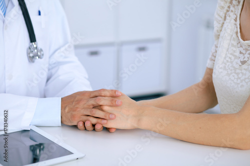 Doctor reassuring his female patient by touching her hands while talking. Symbol of support and trust in medicine