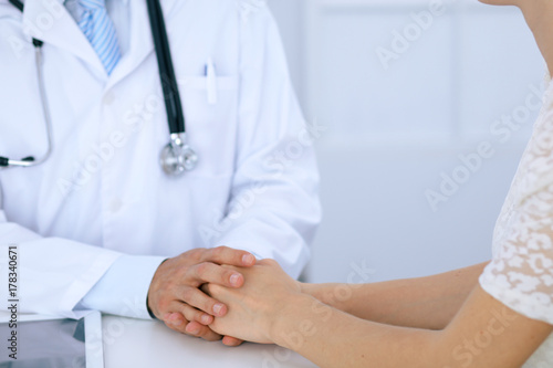 Fototapeta Naklejka Na Ścianę i Meble -  Doctor reassuring his female patient by touching her hands while talking. Symbol of support and trust in medicine