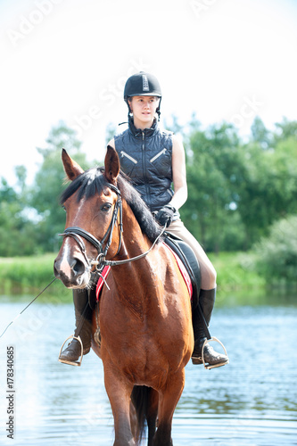 Young teenage girl riding horseback from lake at early morning
