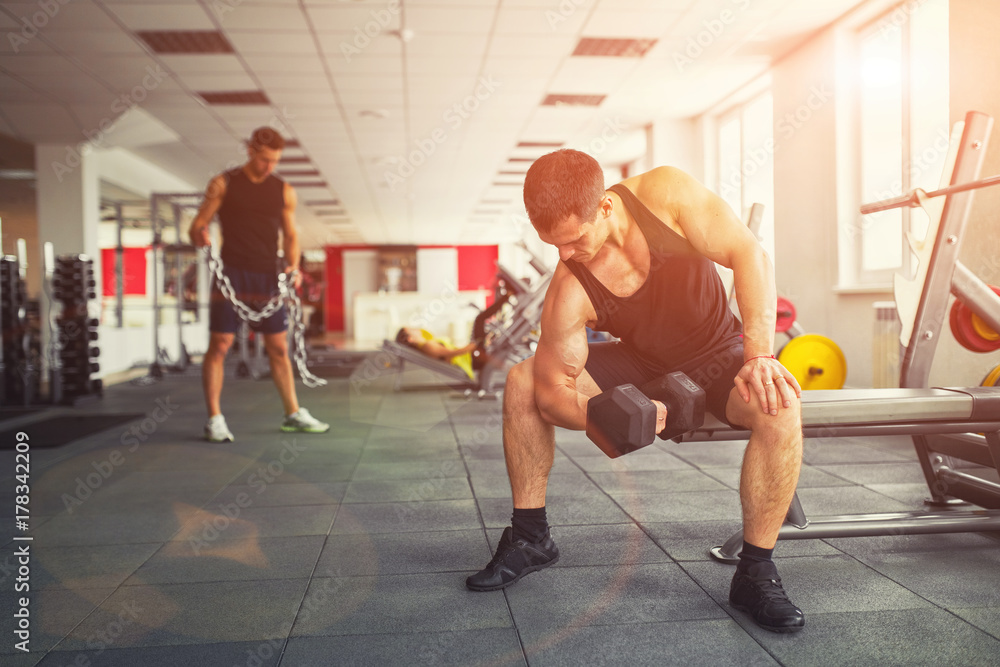 Men train in the gym with dumbbells and chain