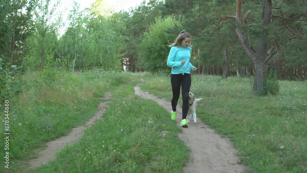 Slender young girl runs through the woods with her thoroughbred dog on warm summer day Slender young girl runs through the woods with her thoroughbred dog on warm summer day