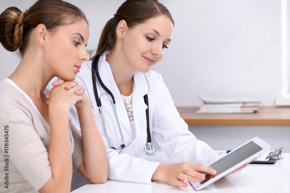 Doctor and patient sitting at the desk. Physician pointing into laptop computer. Medicine and health care concept Doctor and patient sitting at the desk. Physician pointing into laptop computer. Medicine and health care concept