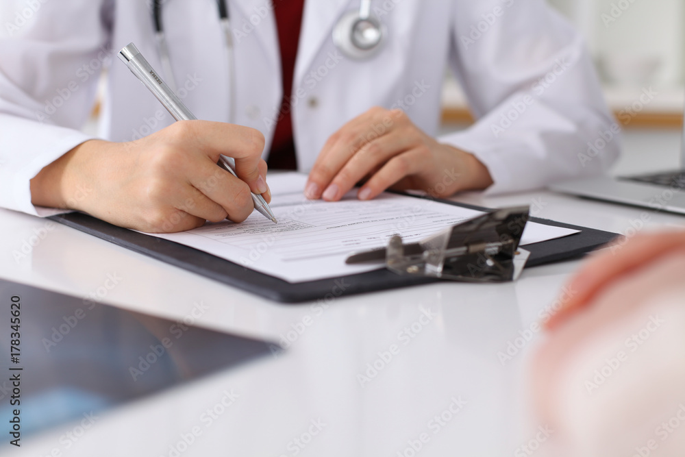 Close up of a female doctor filling up an application form while consulting patient Close up of a female doctor filling up an application form while consulting patient