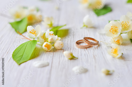 Wedding rings lie on a wooden white background with jasmine branches. Symbol of love and marriage. Bride's traditional symbolic accessory. Floral composition with jasmine flowers.