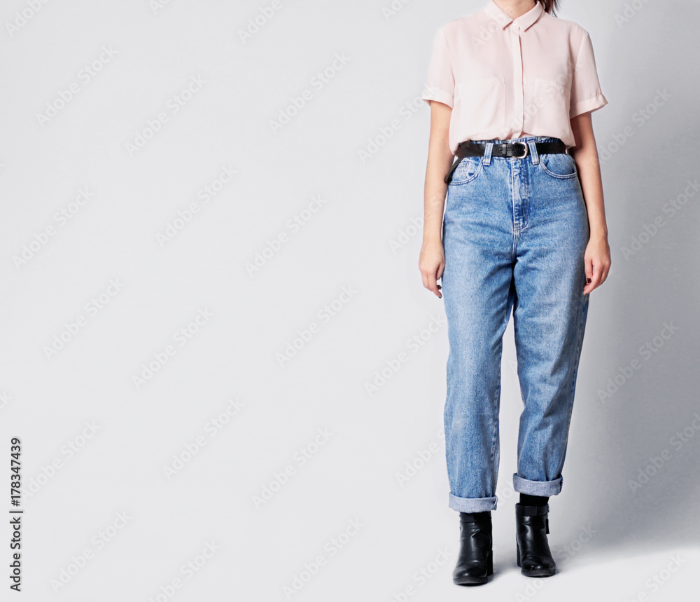 Woman wearing casual outfit with white shirt, blue vintage high-waisted mom  jeans with black ankle boots and black belt isolated on grey background.  Copy space Stock Photo