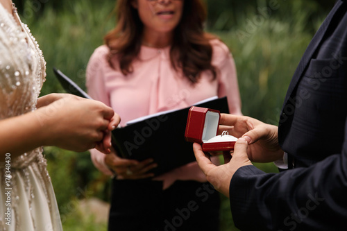 Groom holds wedding rings in red box during wedding ceremony