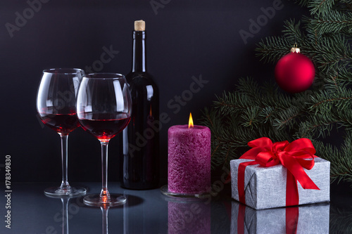Два бокала вина,горящая свеча и новогодний подарок.Фон чёрный.