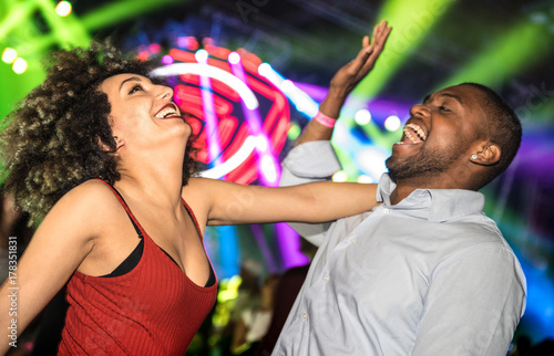 Multiracial young couple dancing at night club with laser light show - Happy people having crazy fun at nightclub after party - Nightlife drunk concept with guy and girl celebrate at concert festival