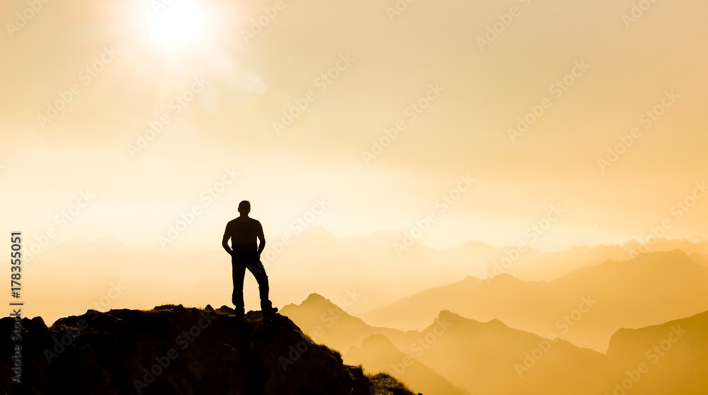 Man reaching summit enjoying freedom and watching towards mountain ranges.