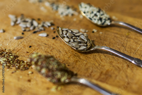 Close up of silver spoons with seeds, chopped linseed, peeled sunflower and sesame on wooden table. Concept of healthy eating.