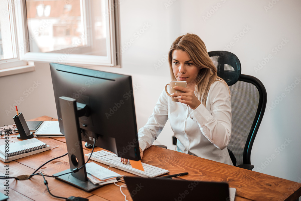 Attractive blonde businesswoman working with computer and drinking coffee in office. Attractive blonde businesswoman working with computer and drinking coffee in office.