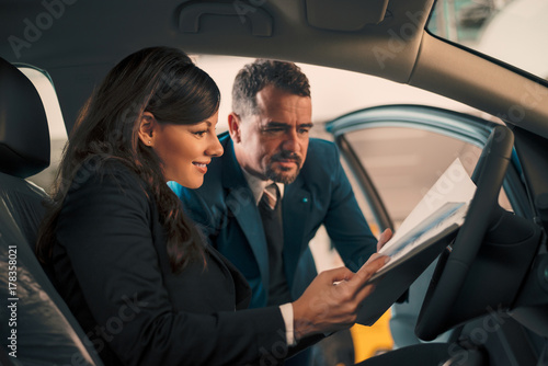 Happy woman inside car in auto salon with car dealer.