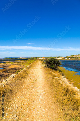 Steiniger Weg entlang an einem Wasserkanal bei der Saline in der kleinen französischen Ortschaft Gruissan in Südfrankreich