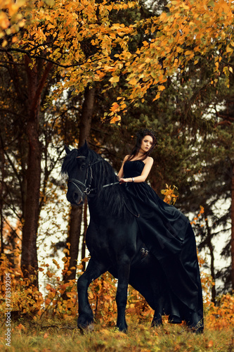 a girl in a black dress and a black tiara on a Frisian horse ride on a magical fairytale forest
