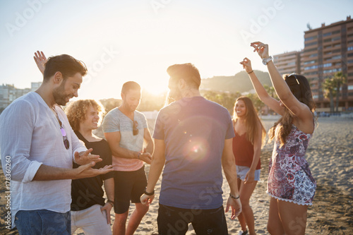 Young man dancing with friends on beach in sunlight
