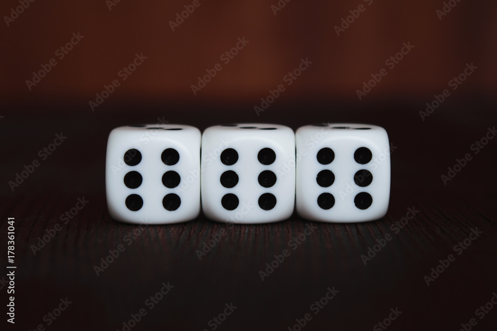 Three white plastic dices in a row on brown wooden board background. Six sides cube with black dots. Satan number 666. Three white plastic dices in a row on brown wooden board background. Six sides cube with black dots. Satan number 666.