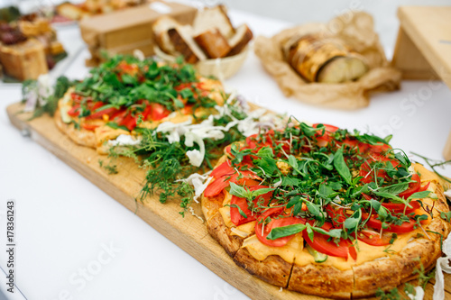 Pizza with many tomatoes and greenery served on wooden board