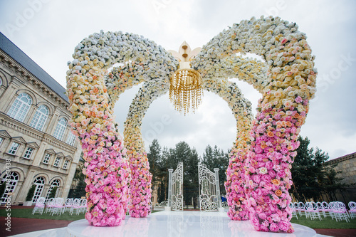 Wedding altar made of archs of pink, yellow and white flowers stands on the backyard